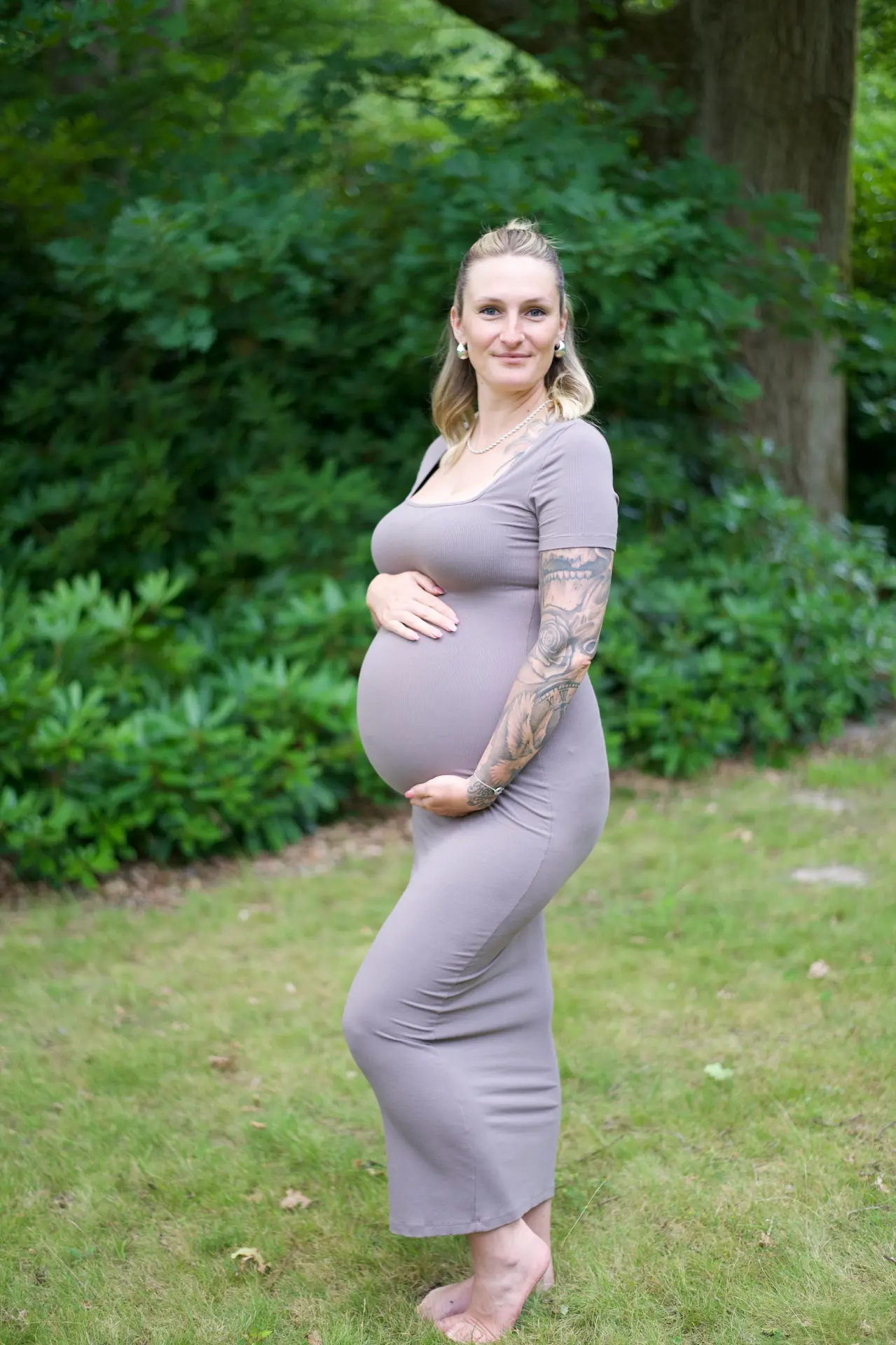 Babybauch-Shooting in der Natur – Frau hält glücklich ihren Babybauch.