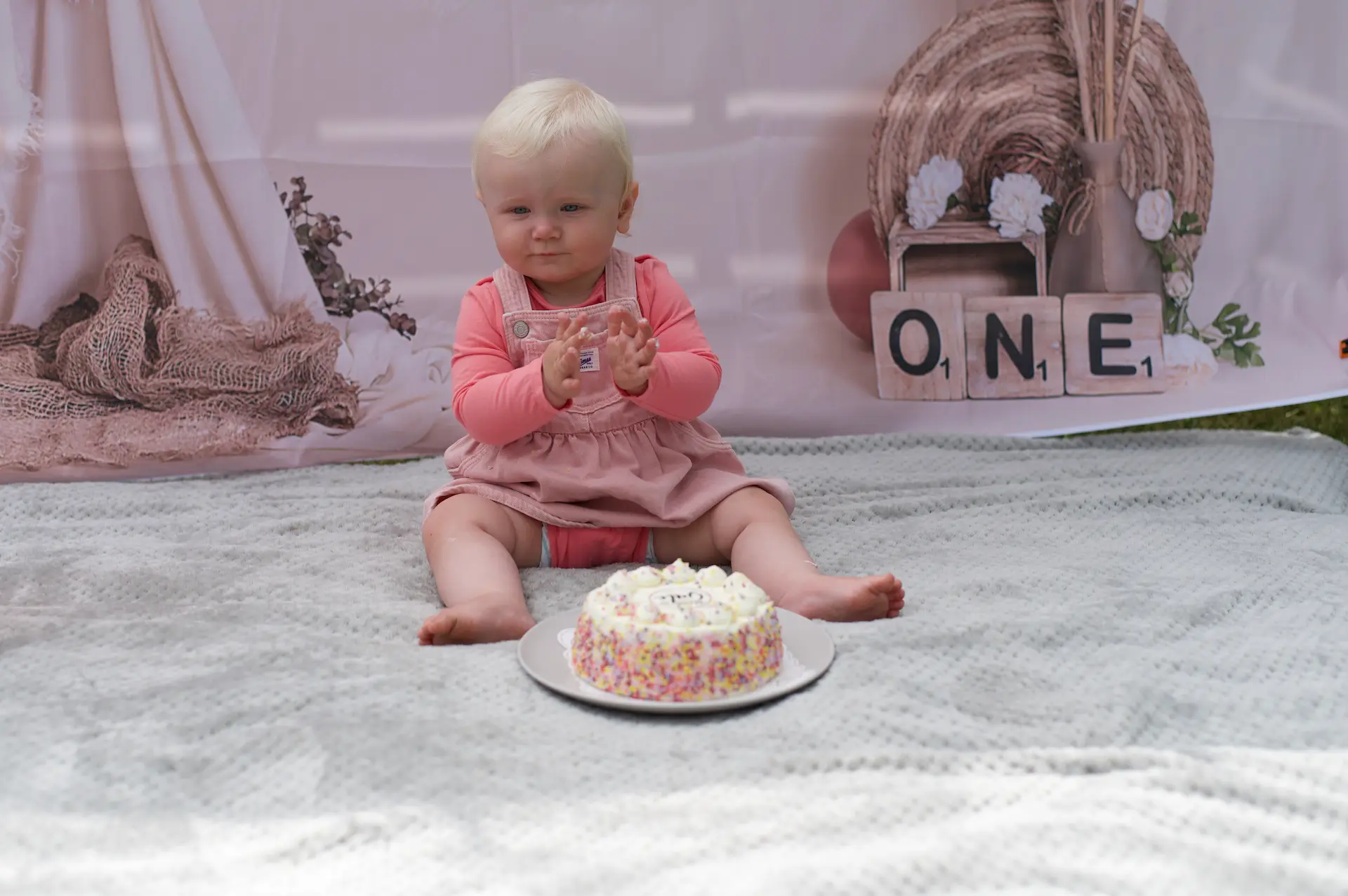 Baby klatscht in die Hände und freut sich auf die vor sich stehende Geburtstagstorte.