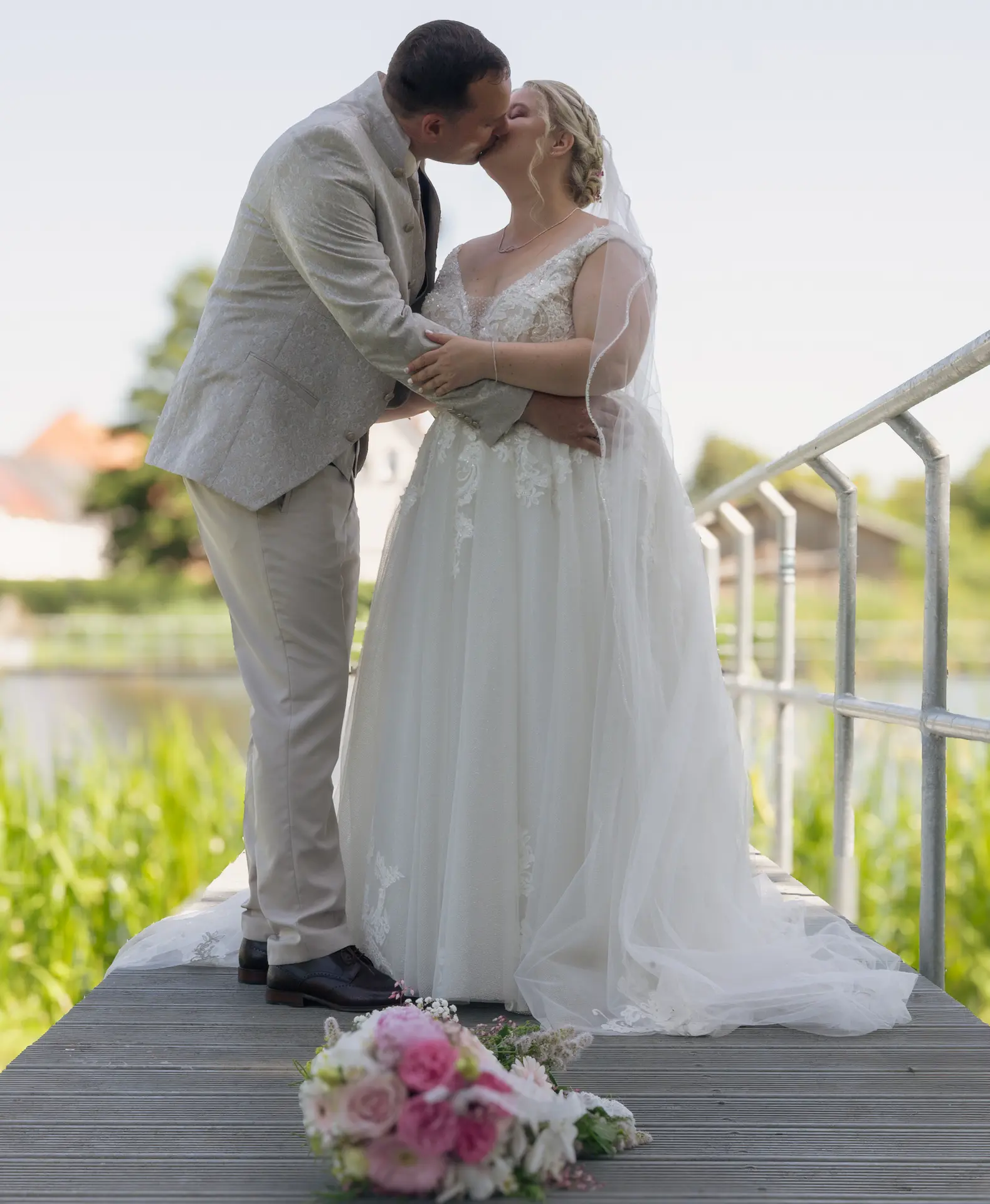 Hochzeitspaar küsst sich auf einem Steg am See.