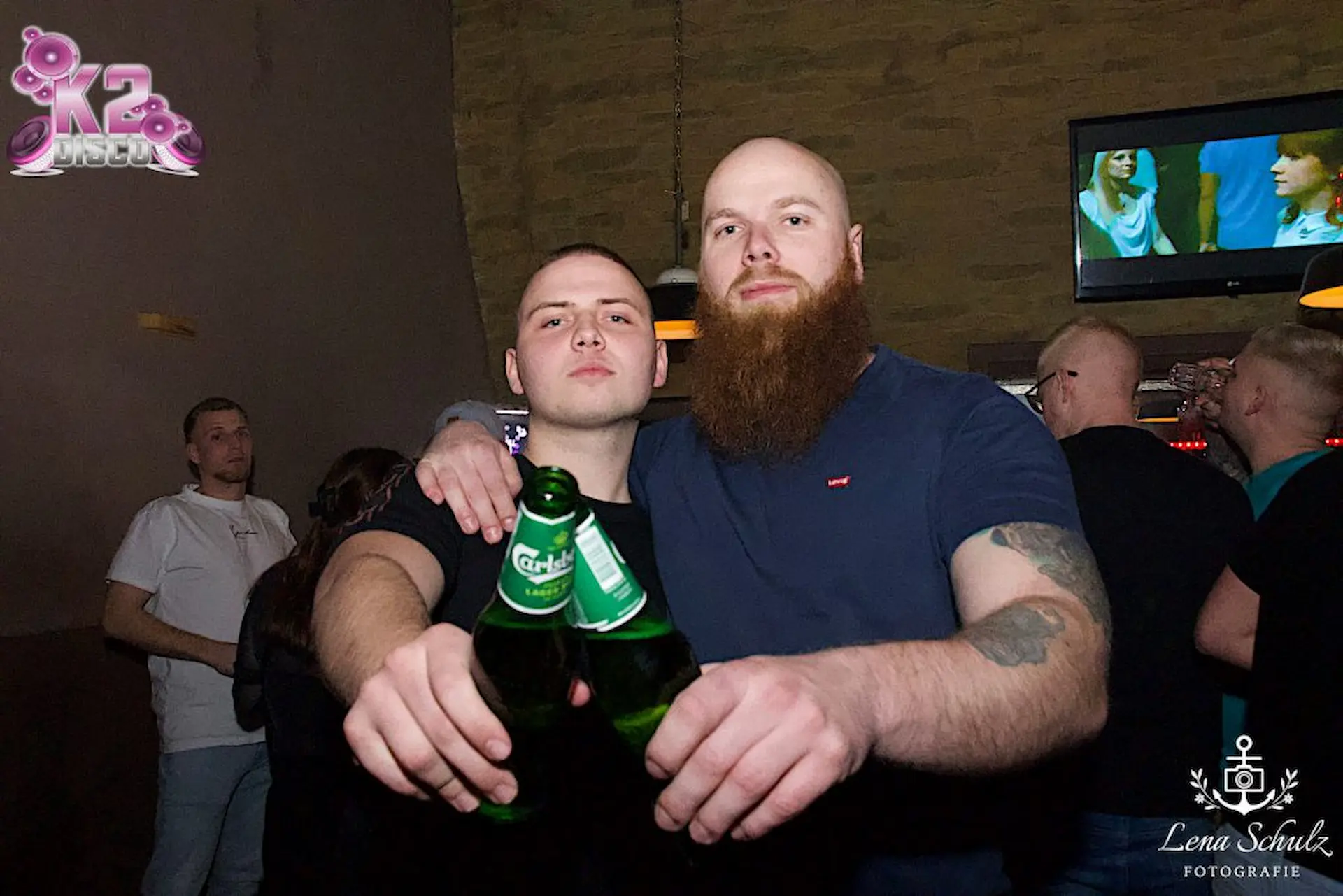Event-Fotografie: Zwei Freunde stoßen bei einer Veranstaltung im K2 mit ihrem Bier an.